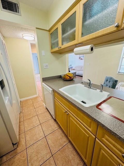 kitchen featuring white appliances, a sink, light tile patterned floors, glass insert cabinets, and brown cabinetry