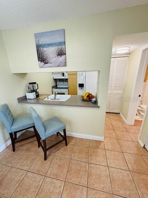 office with a textured ceiling, light tile patterned floors, a sink, and baseboards
