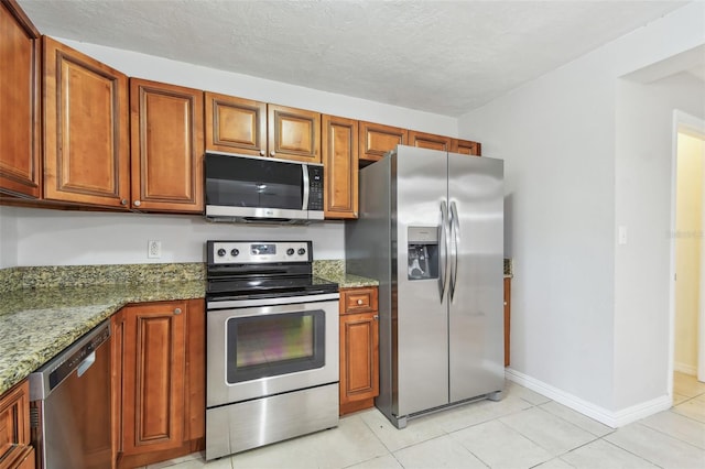 5010 8th Ave N, Saint Petersburg, FL 33710 - kitchen featuring stainless steel appliances, light tile patterned floors, brown cabinets, stone countertops, and baseboards
