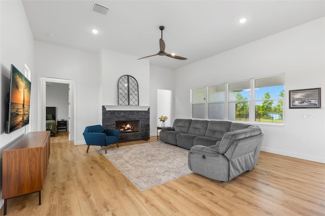 living room featuring ceiling fan, light wood-style floors, baseboards, a stone fireplace, and recessed lighting