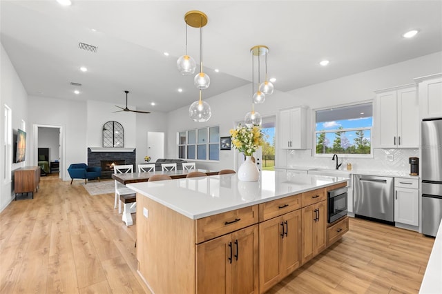 kitchen with appliances with stainless steel finishes, ceiling fan, a fireplace, backsplash, and light wood finished floors