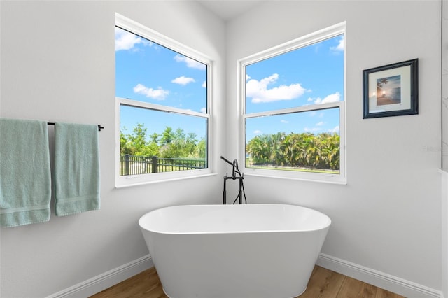 full bath with baseboards, wood finished floors, and a freestanding bath