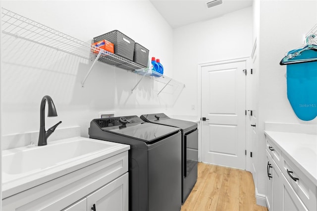 laundry area with washing machine and clothes dryer, light wood-style flooring, and cabinet space