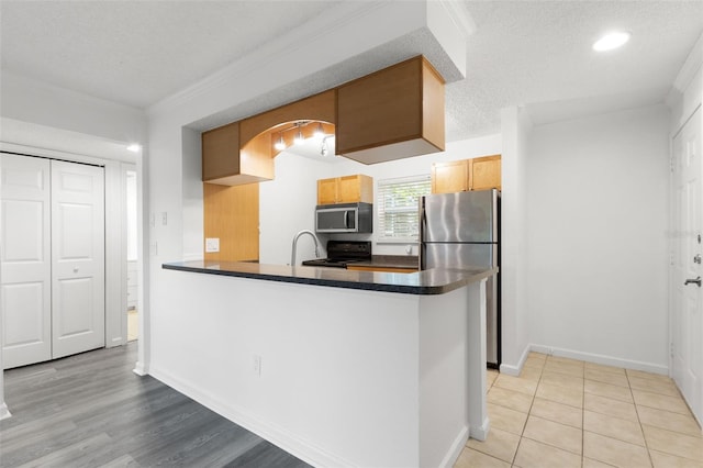 2500 Winding Creek Blvd Unit A104, Clearwater, FL 33761 - kitchen with appliances with stainless steel finishes, dark countertops, crown molding, a textured ceiling, and a peninsula