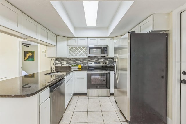 kitchen featuring appliances with stainless steel finishes, a sink, a peninsula, white cabinets, and light tile patterned floors