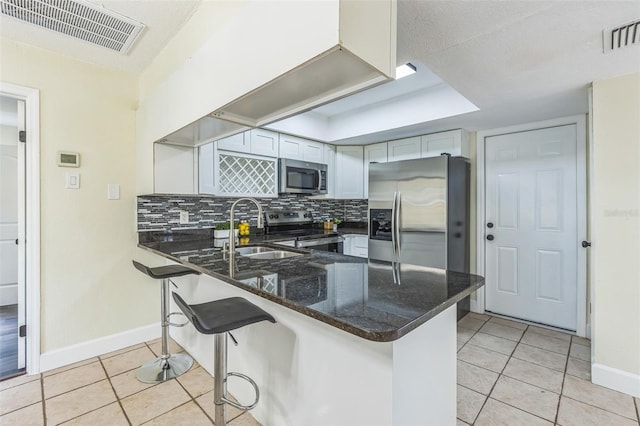 kitchen with stainless steel appliances, a sink, light tile patterned flooring, and a peninsula