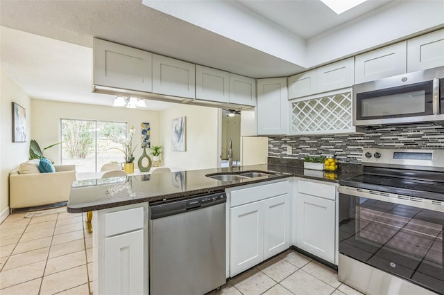kitchen featuring appliances with stainless steel finishes, a sink, light tile patterned floors, a peninsula, and dark stone counters