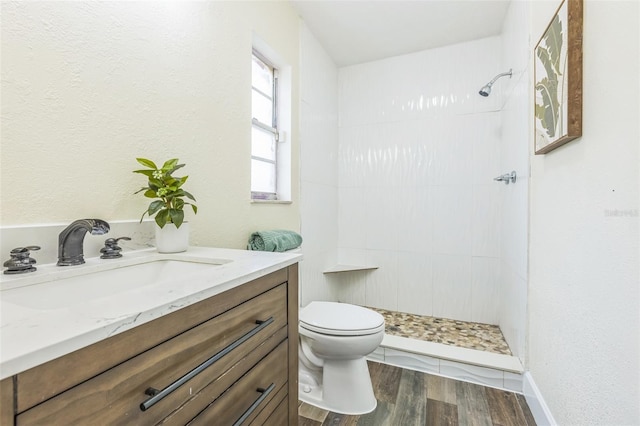 bathroom featuring a tile shower, toilet, wood finished floors, and vanity