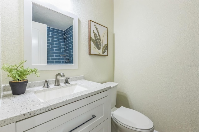 bathroom featuring a textured wall, vanity, and toilet
