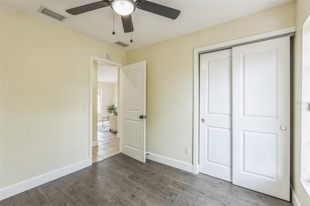 unfurnished bedroom with baseboards, a closet, dark wood-style flooring, and a ceiling fan