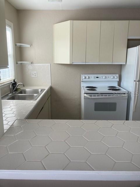 556 Virginia St, Dunedin, FL 34698 - kitchen with white appliances, a sink, tile counters, open shelves, and white cabinets