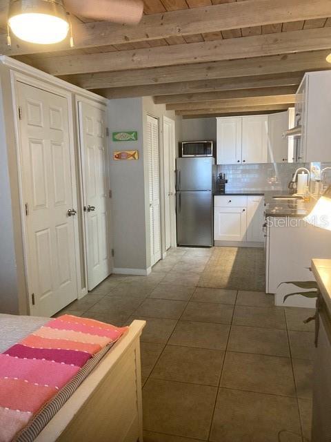 556 Virginia St, Dunedin, FL 34698 - kitchen with stainless steel appliances, white cabinets, a sink, beamed ceiling, and tasteful backsplash