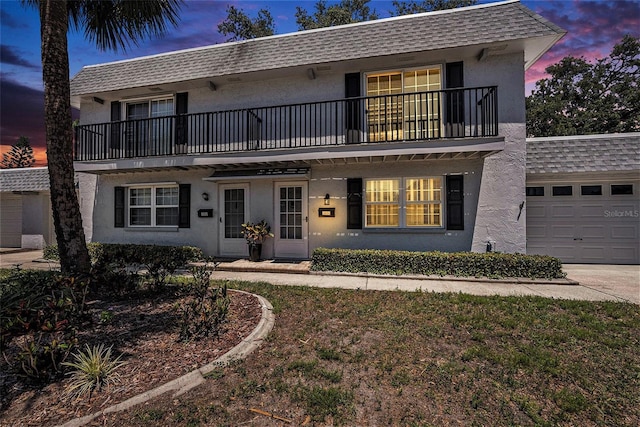 front facade featuring a balcony, stucco siding, an attached garage, and roof with shingles