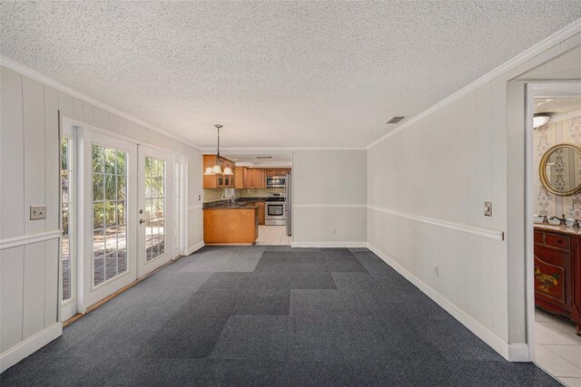 unfurnished living room featuring crown molding, french doors, a textured ceiling, baseboards, and a sink