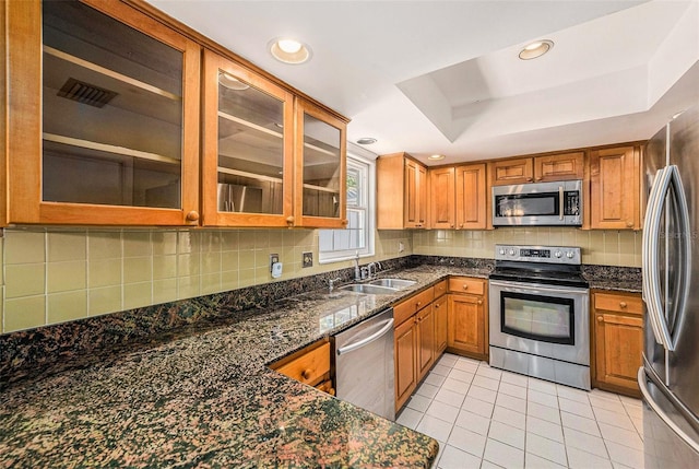 kitchen featuring appliances with stainless steel finishes, a sink, light tile patterned flooring, decorative backsplash, and brown cabinetry