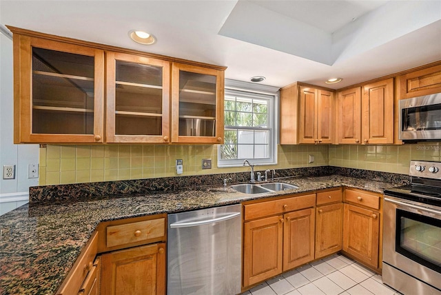 kitchen featuring stainless steel appliances, a sink, decorative backsplash, dark stone counters, and recessed lighting
