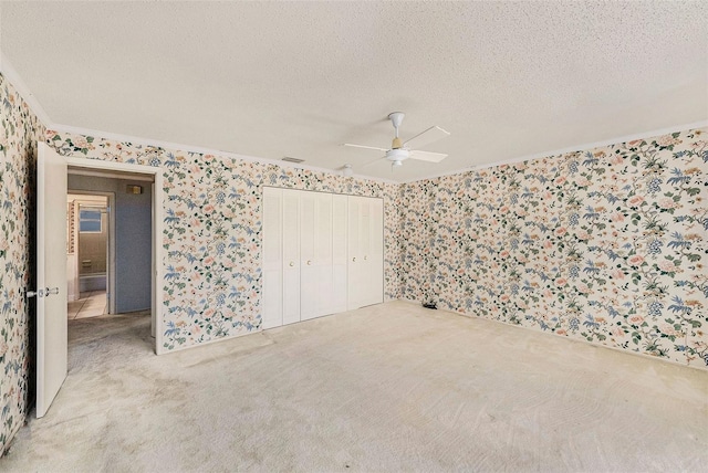 unfurnished bedroom featuring wallpapered walls, carpet floors, ornamental molding, a textured ceiling, and a closet
