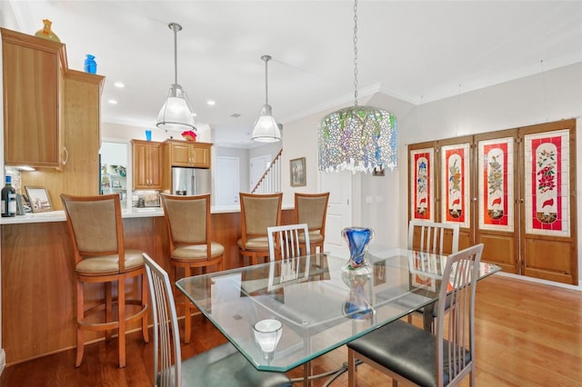dining area with light wood-style flooring, ornamental molding, and stairway