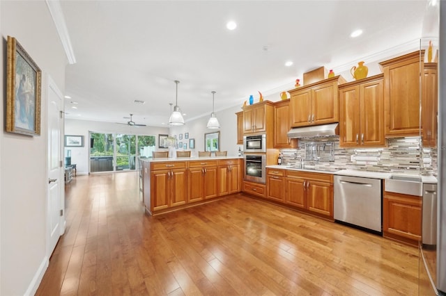 kitchen with stainless steel appliances, under cabinet range hood, a peninsula, crown molding, and light countertops