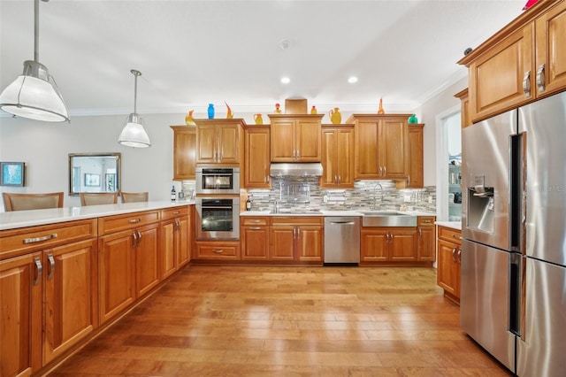 kitchen with appliances with stainless steel finishes, a sink, crown molding, brown cabinets, and light countertops