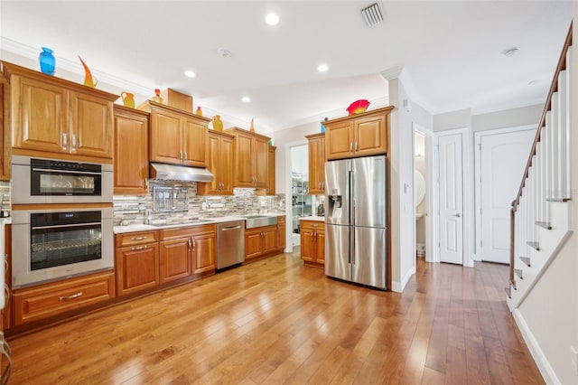 kitchen with appliances with stainless steel finishes, ornamental molding, tasteful backsplash, brown cabinetry, and light countertops