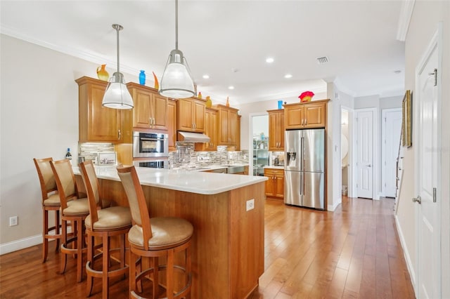 kitchen featuring stainless steel appliances, a peninsula, under cabinet range hood, ornamental molding, and backsplash