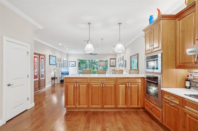 kitchen featuring a peninsula, ornamental molding, light countertops, light wood-type flooring, and pendant lighting