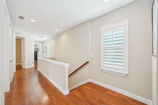 hall with an upstairs landing, light wood-style floors, recessed lighting, and baseboards