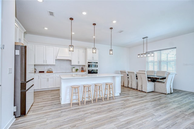 kitchen featuring freestanding refrigerator, custom exhaust hood, light wood-style flooring, backsplash, and white cabinets