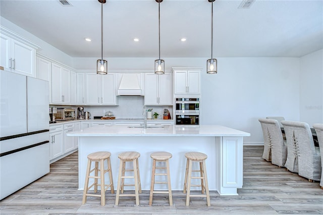 kitchen featuring freestanding refrigerator, a sink, custom range hood, recessed lighting, and white cabinetry