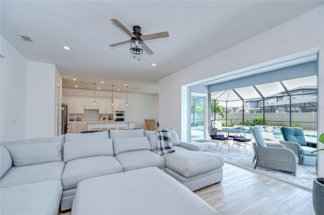 living room featuring ceiling fan, light wood-style floors, a sunroom, and recessed lighting