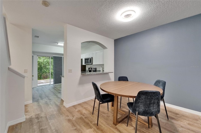 15855 Fishhawk View Dr, Lithia, FL 33547 - dining space featuring light wood finished floors, a textured ceiling, arched walkways, and baseboards