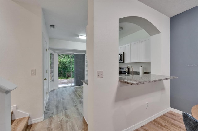 15855 Fishhawk View Dr, Lithia, FL 33547 - kitchen with stainless steel microwave, white cabinetry, light stone countertops, light wood-type flooring, and a sink