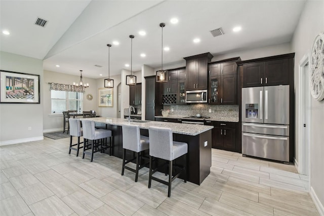 kitchen with appliances with stainless steel finishes, backsplash, a large island with sink, a kitchen breakfast bar, and baseboards