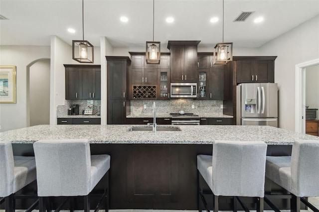 kitchen with appliances with stainless steel finishes, a sink, tasteful backsplash, dark brown cabinets, and recessed lighting