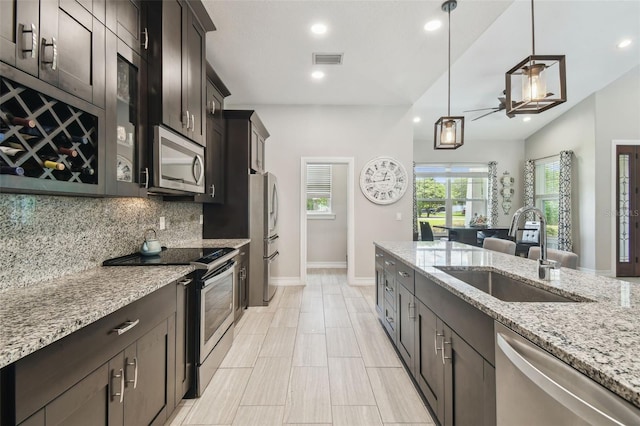 kitchen with appliances with stainless steel finishes, a sink, decorative backsplash, pendant lighting, and light stone counters