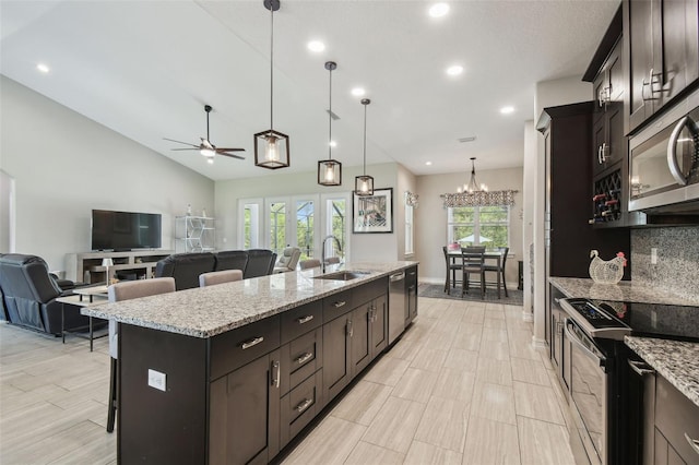 kitchen featuring a sink, appliances with stainless steel finishes, a kitchen island with sink, ceiling fan, and a breakfast bar area