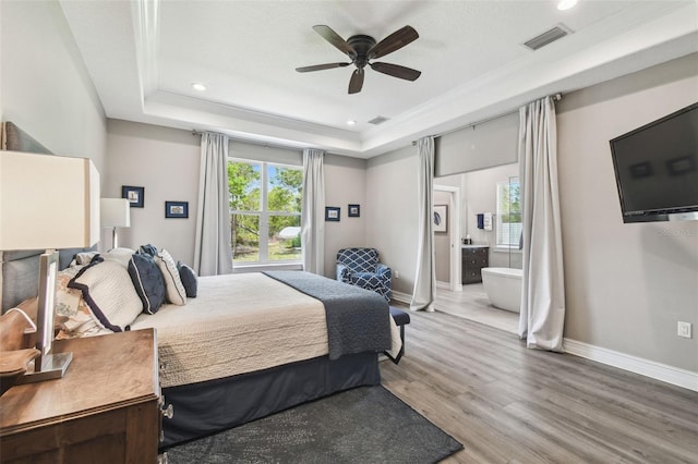 bedroom with a tray ceiling, light wood-style floors, baseboards, connected bathroom, and recessed lighting
