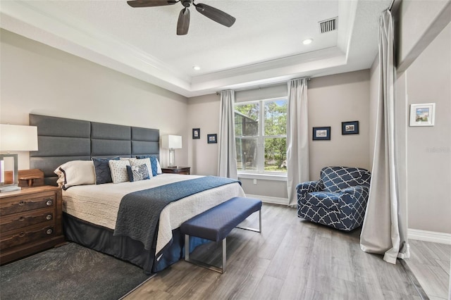 bedroom featuring a raised ceiling, baseboards, wood finished floors, recessed lighting, and crown molding