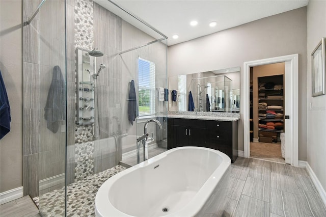 bathroom featuring a stall shower, a soaking tub, vanity, a walk in closet, and baseboards