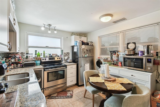 361 Colonial Ct, Dunedin, FL 34698 - kitchen with appliances with stainless steel finishes, a sink, white cabinetry, light tile patterned floors, and light stone counters
