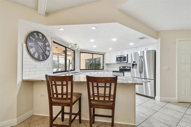 854 Village Way, Palm Harbor, FL 34683 - kitchen with appliances with stainless steel finishes, a peninsula, a sink, light stone counters, and white cabinetry