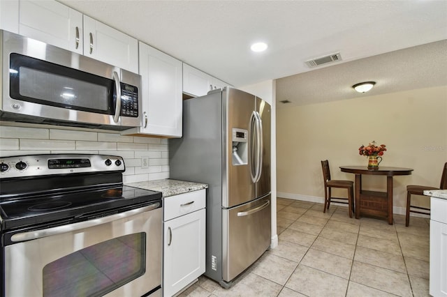 854 Village Way, Palm Harbor, FL 34683 - kitchen with stainless steel appliances, white cabinetry, backsplash, light tile patterned flooring, and baseboards
