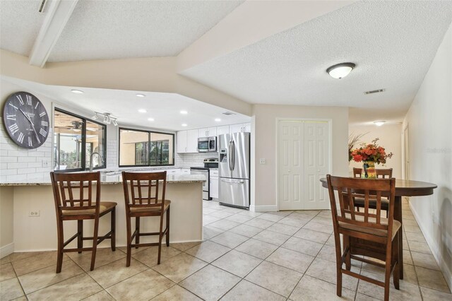 854 Village Way, Palm Harbor, FL 34683 - kitchen with stainless steel appliances, a textured ceiling, a peninsula, tasteful backsplash, and light tile patterned floors