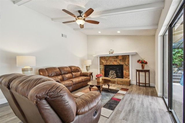 854 Village Way, Palm Harbor, FL 34683 - living area with beam ceiling, light wood-type flooring, a textured ceiling, ceiling fan, and a stone fireplace