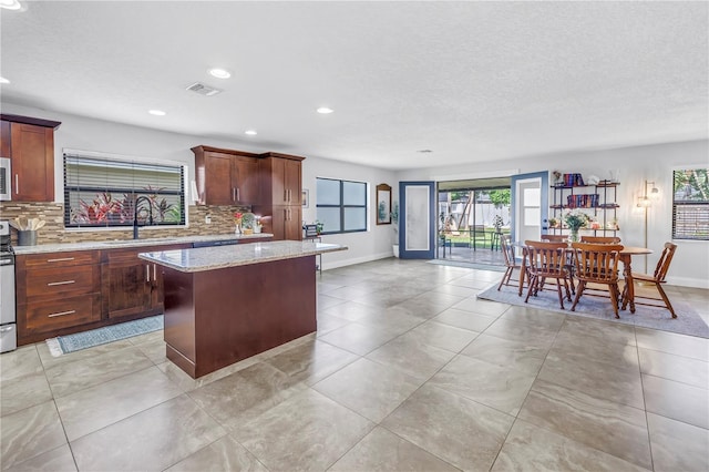 4821 S Gachet Blvd, Lakeland, FL 33813 - kitchen with a sink, backsplash, a kitchen island, baseboards, and light stone counters