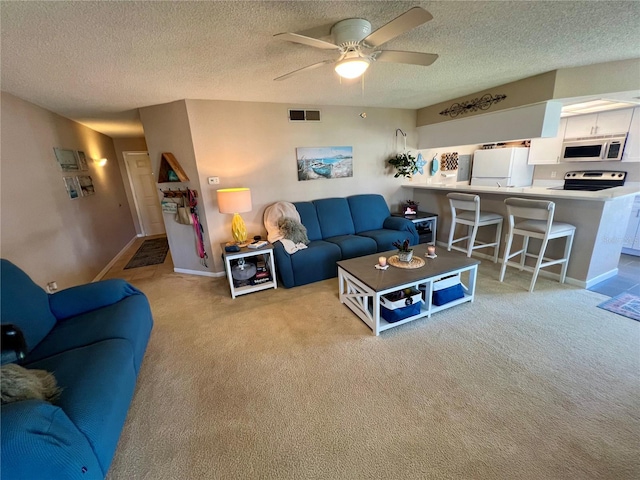 living room with a textured ceiling, light carpet, a ceiling fan, and baseboards