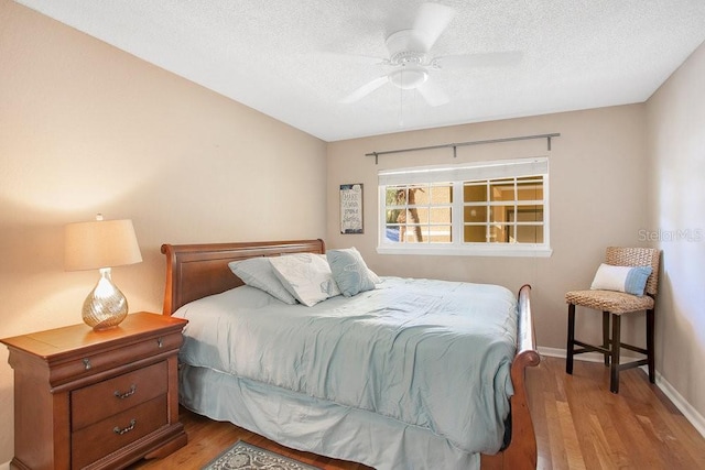 bedroom featuring wood finished floors, a textured ceiling, baseboards, and a ceiling fan