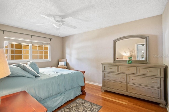bedroom featuring light wood-style floors, baseboards, a textured ceiling, and ceiling fan