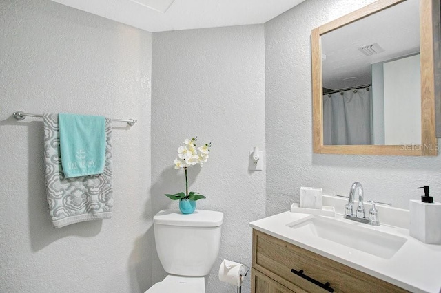 bathroom featuring a textured wall, vanity, and toilet